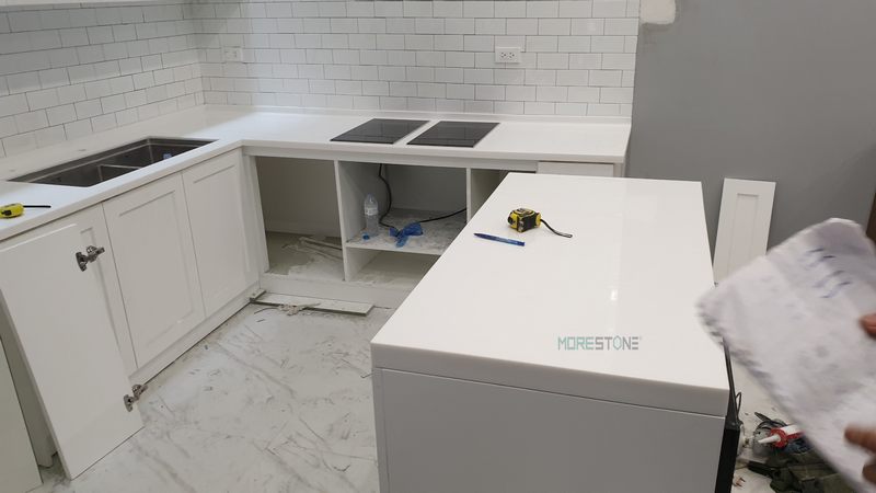 Tủ bếp được ốp bằng đá nhân tạo màu trắng có ưu điểm uốn nắn tuyệt vời, không để lại mấu nối một mạch liền nhau, giúp tăng thêm tính thẩm mỹ cao.